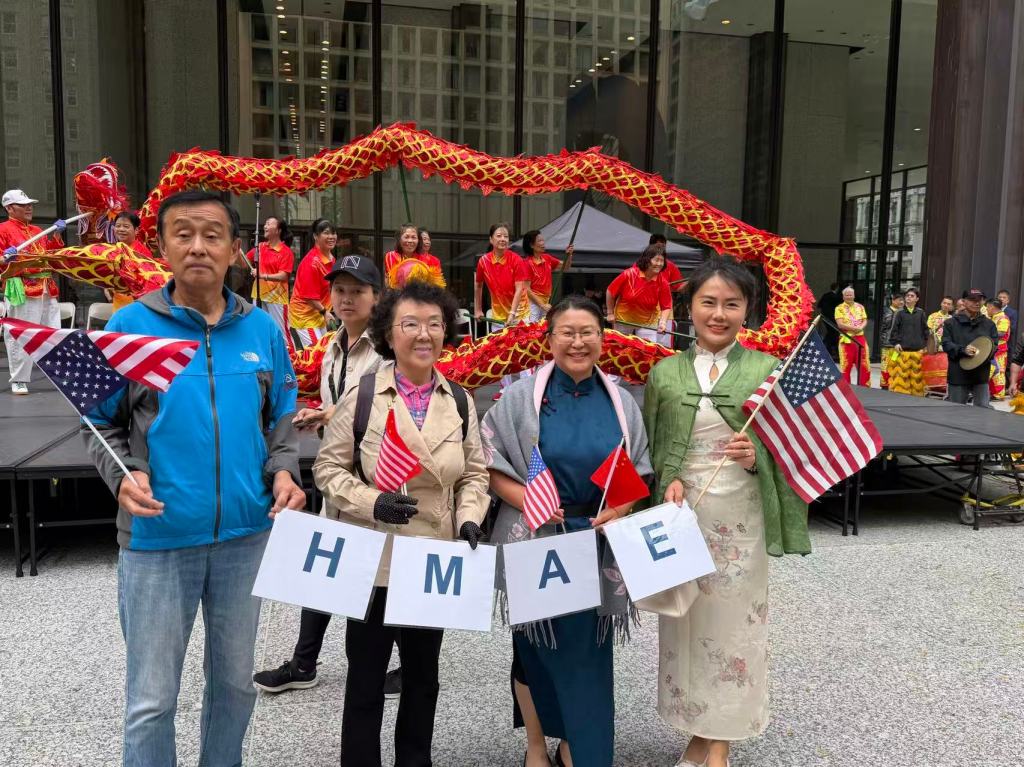 Four HMAE members holding HMAE letter signs in front of a traditional Chinese dragon dance at Chicago's Daley Plaza.